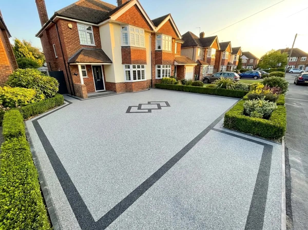 A newly installed light grey resin driveway with dark grey borders and a central pattern in front of a traditional brick house.